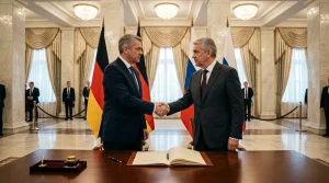 Zwei Politiker schütteln sich die Hand vor deutschen und russischen Flaggen.